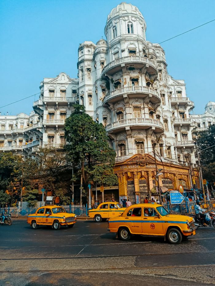 View of yellow taxis and vibrant city life in front of Kolkata's historic city architecture.