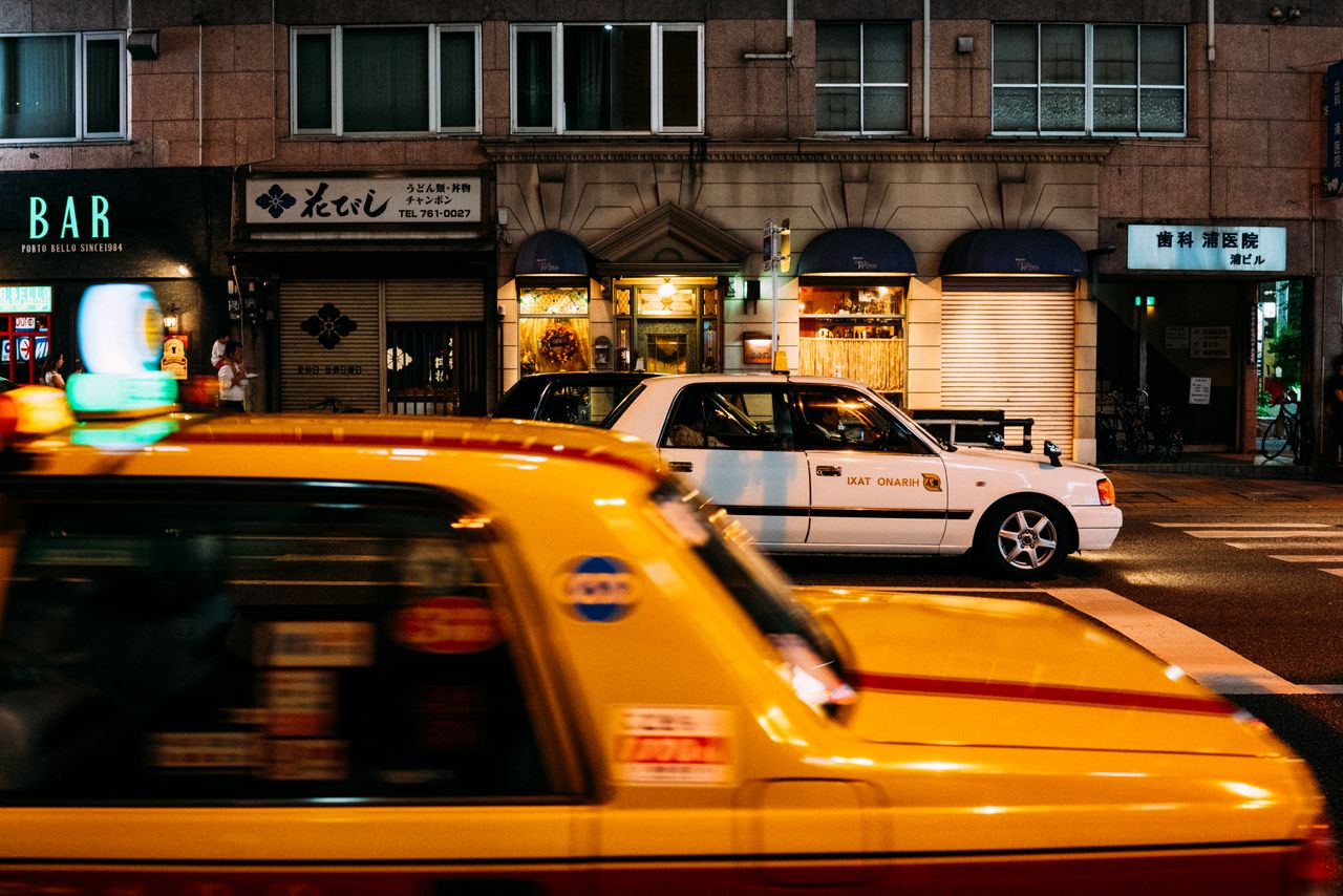 Services Dynamic Tokyo street scene featuring yellow taxis and illuminated storefronts at night.